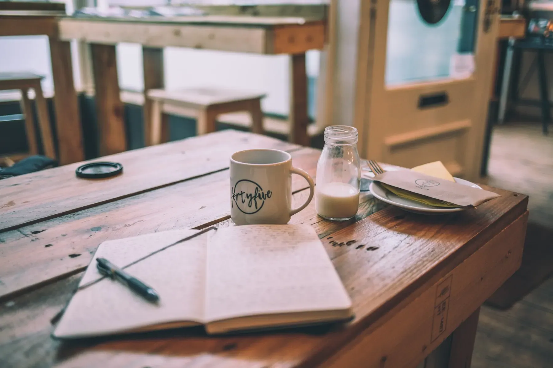 Cuaderno abierto y taza de café sobre mesa de madera en ambiente cosmopolita