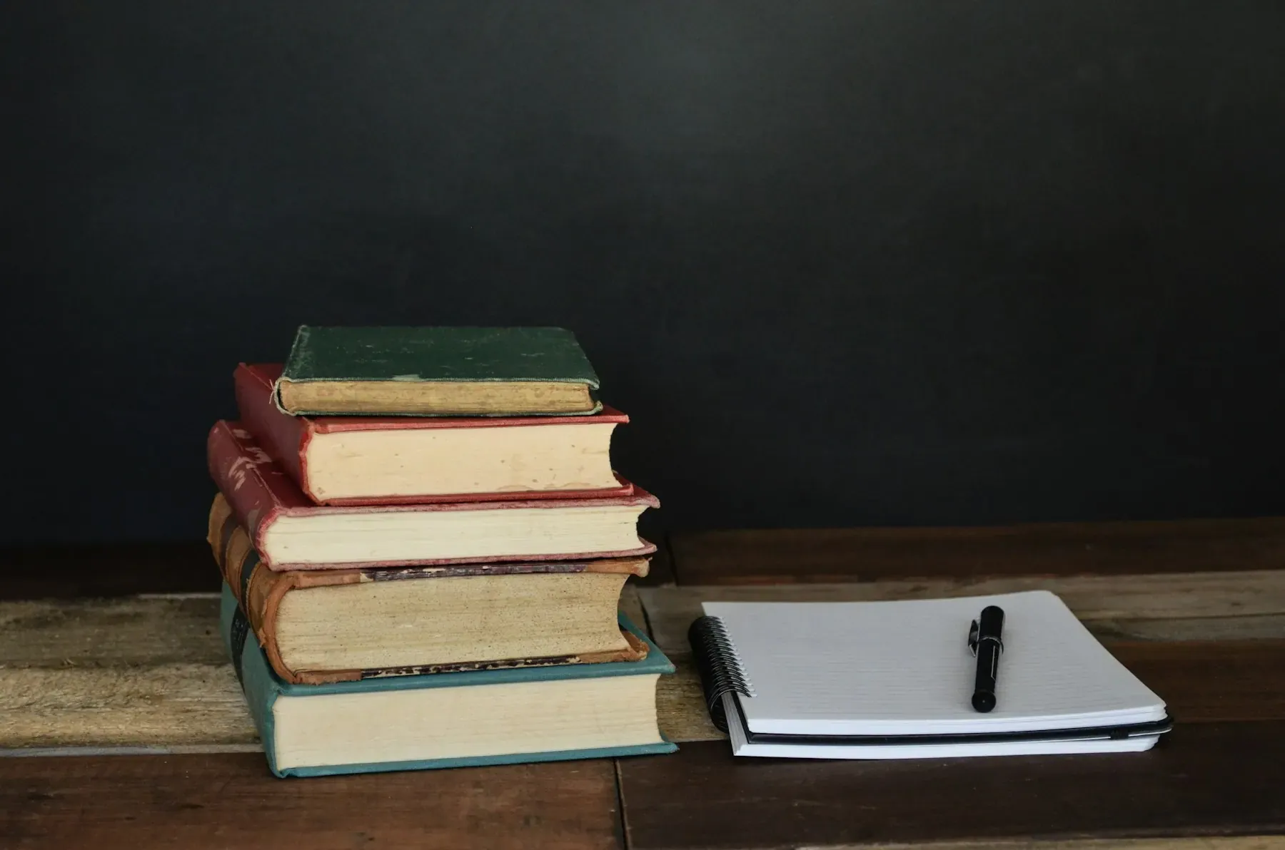 Pila de libros antiguos encuadernados en tela con libreta y pluma al lado